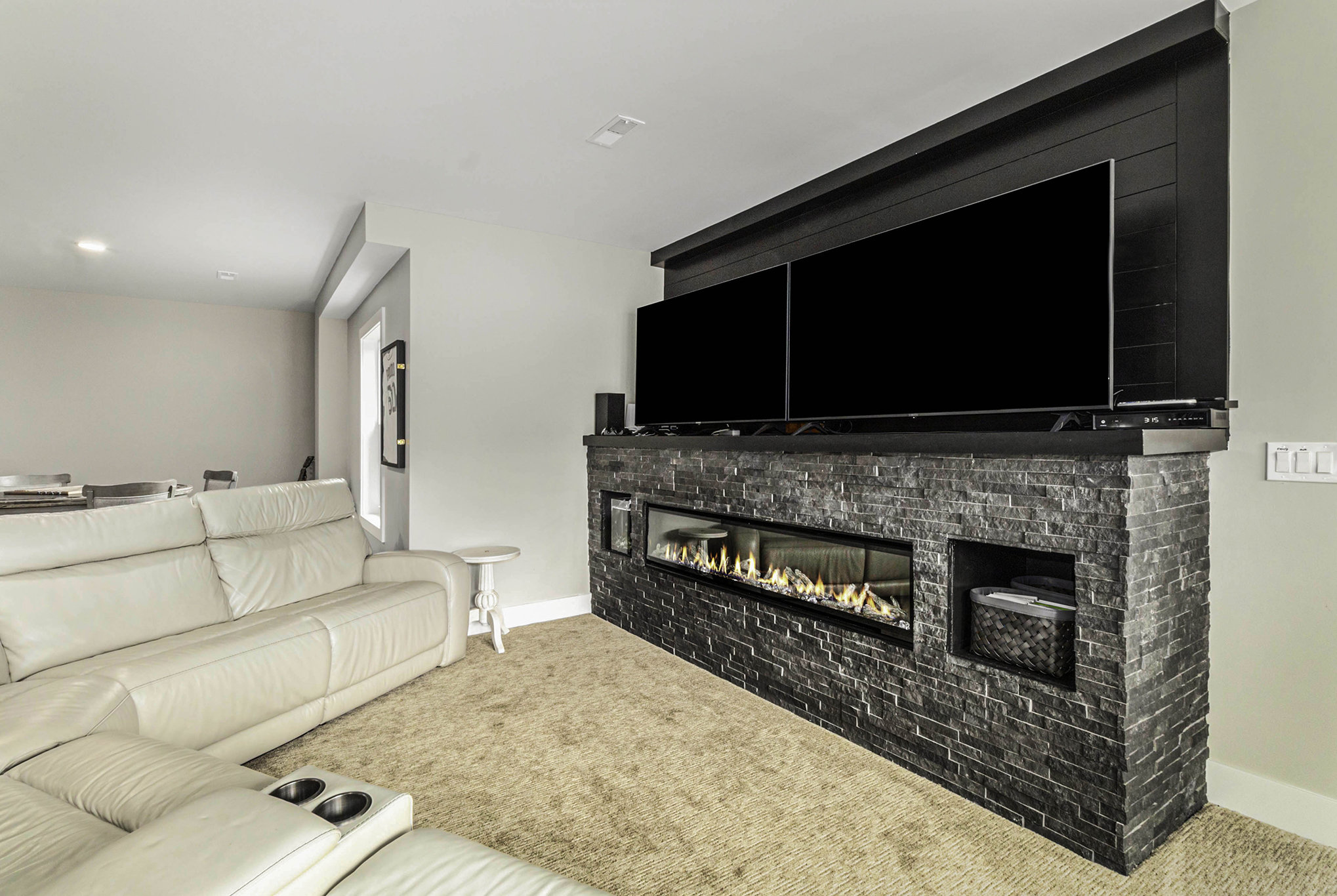 Basement entertainment area with stacked stone fireplace and dual TVs
