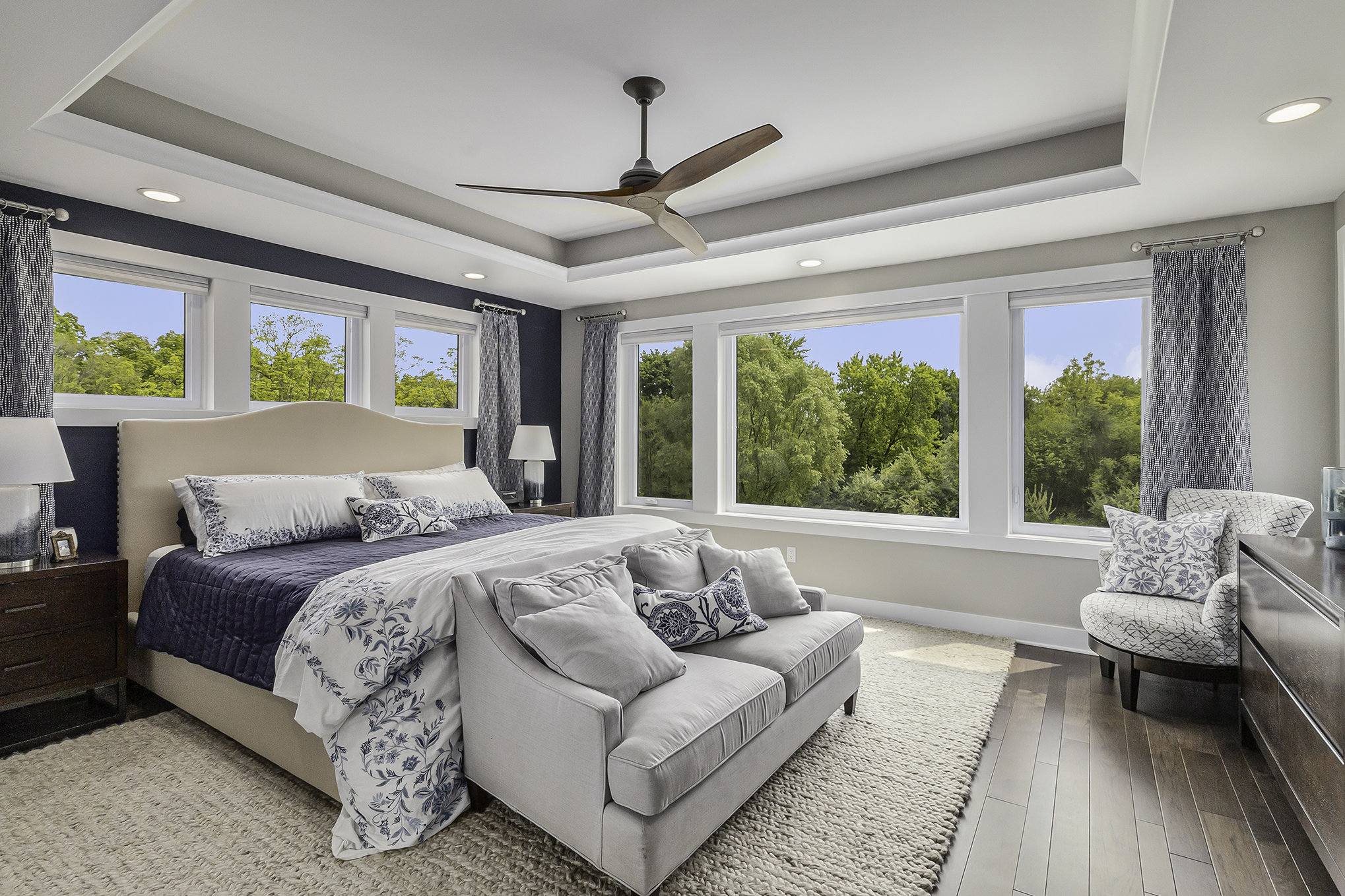 Primary bedroom with navy accent wall, tray ceiling, and forest views