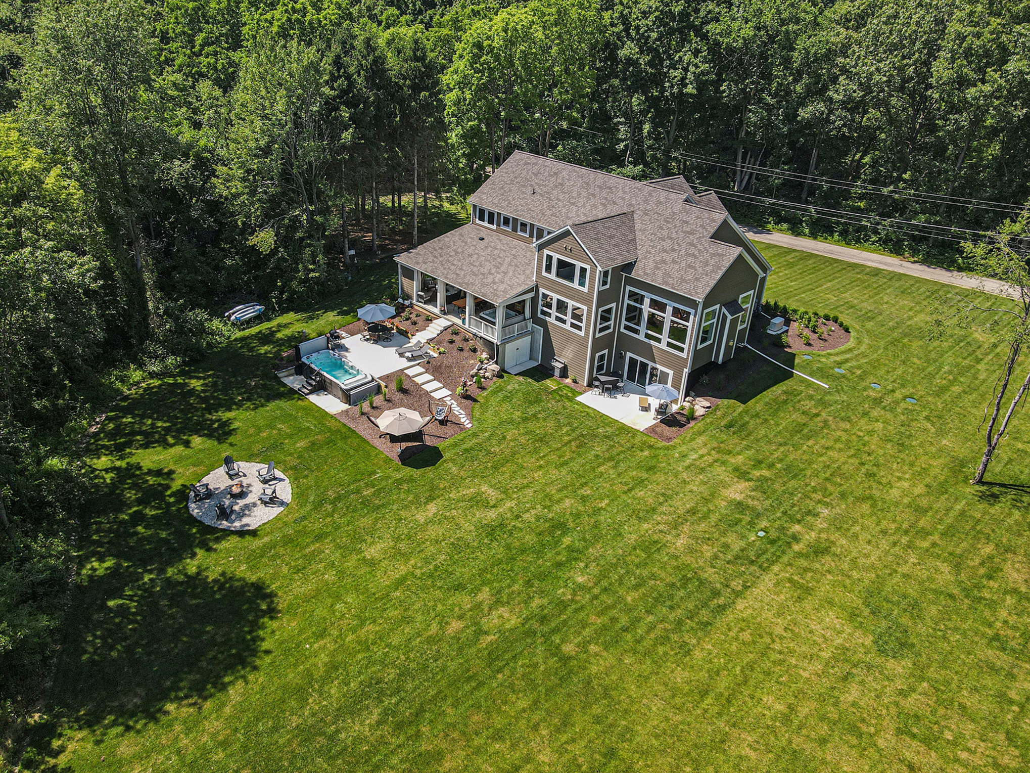 Aerial drone view of the home, surrounding woods, patios, hot tub, and fire pit on the property