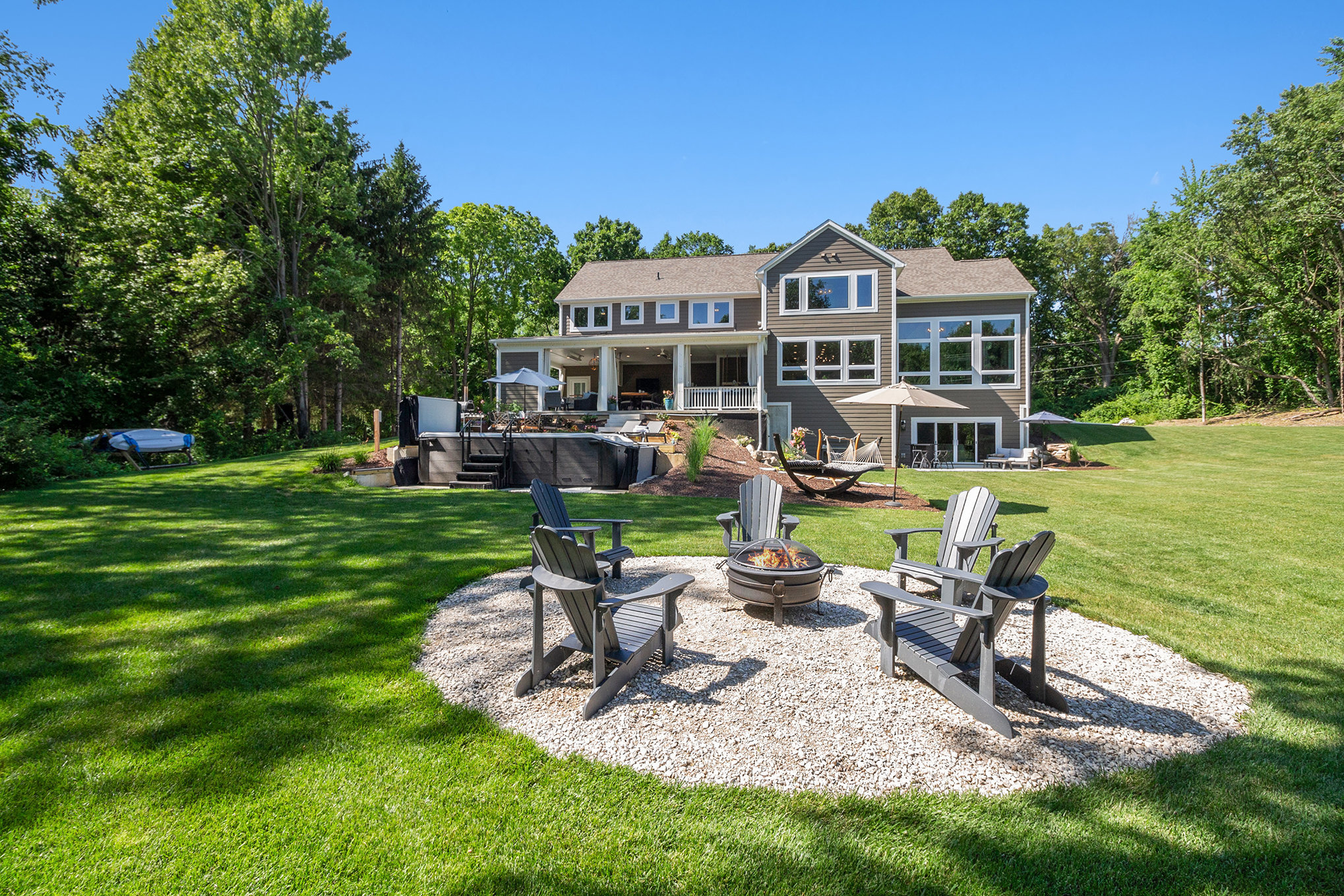 Covered four-season patio with stone fireplace, live-edge bar, hot tub, and forest views